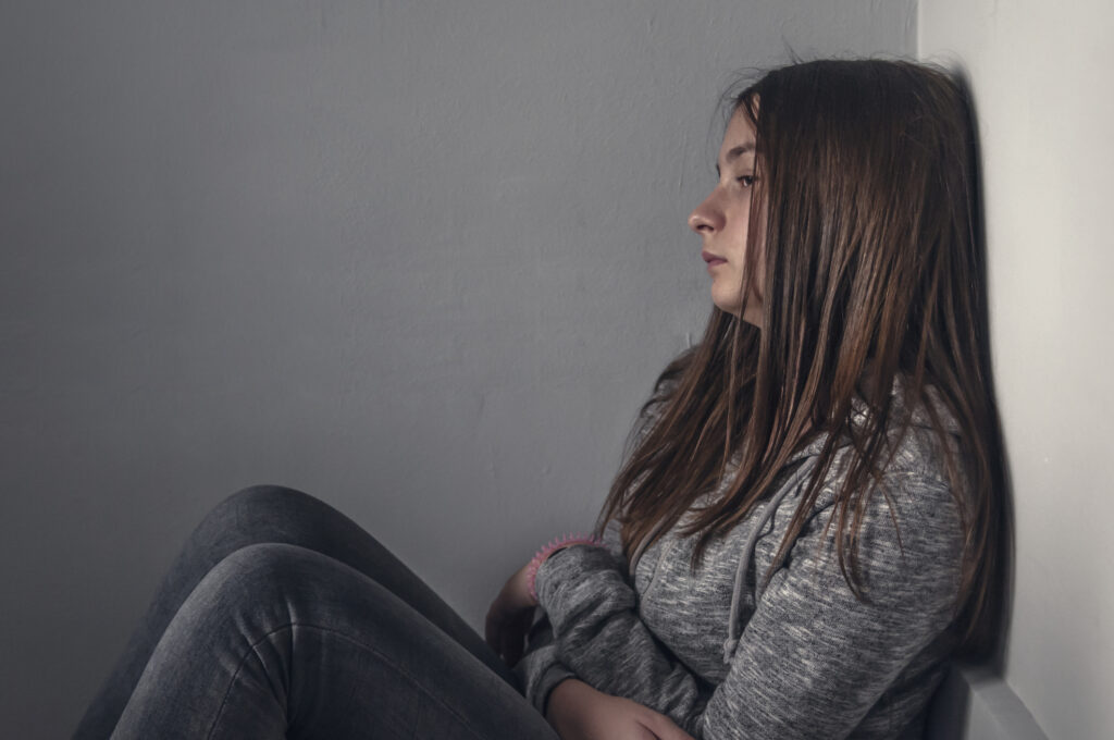 Sad girl sitting on the floor in corner of room,  portrait of a sad teenage girl looking thoughtful about troubles. Depressed teenage girl. Lonely Depressed Teen Girl. Unhappy depressed teenager