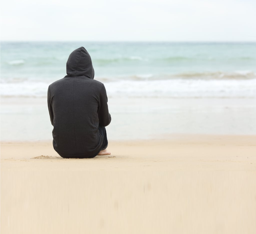 male sitting alone on a beach wearing a hoody